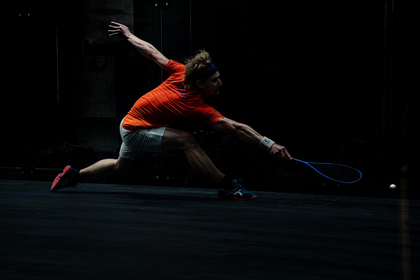 Player lunging low under dramatic spotlight on a dark court